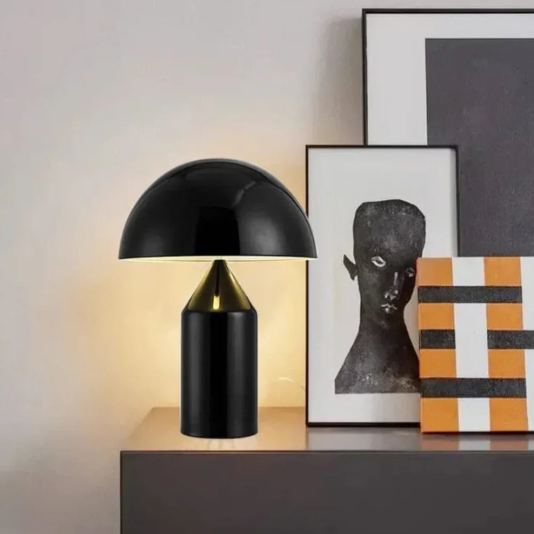 Black table lamp on a wooden surface with framed artwork in the background